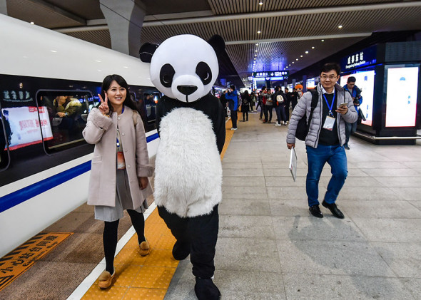A passenger poses for a photo with a performer in a panda costume at Chengdu East Railway Station in Sichuan province on Wednesday. The Xi'an-Chengdu high-speed railway opened on Wednesday. ��Lyu Jia / For China Daily��