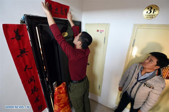 Xu Cun's son Huang Yubin (L) and a friend paste couplets at Xu's new apartment in a relocation community in Gulang, Northwest China's Gansu province, Feb 7, 2018. Xu Cun, with a disabled husband ill in bed and mother-in-law over 70, is the backbone of her family. ��Photo/Xinhua��
