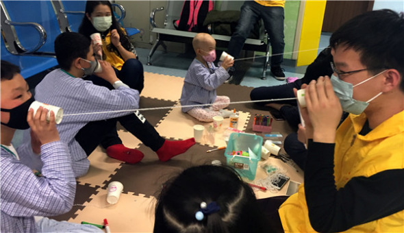 Volunteers help children to use telephones made from paper cups and string to explain how sound waves move. (YUAN QUAN/XINHUA)