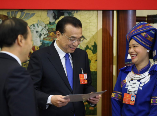 Premier Li Keqiang examines photos presented by Wei Zhaohui, a deputy from the Guangxi Zhuang autonomous region (right), on Tuesday. The photos show major changes in Wei��s home village. Li joined a group discussion with the delegation. (Photo/China Daily)